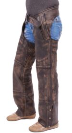Someone stands against a white background wearing 4 Pocket Vintage Brown Leather Chaps Removable Lining over ripped blue denim shorts and tan sneakers.