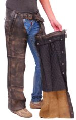 Wearing jeans and brown shoes, a person holds open the 4 Pocket Vintage Brown Leather Chaps Removable Lining, displaying the quilted interior and how they fit over pants.
