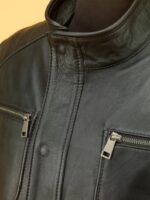 Black leather jacket with multiple zippers and high collar displayed on stand against beige background.
