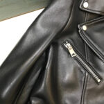 Black leather biker jacket featuring angular pockets, silver buttons, and a waist buckle.