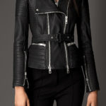 A woman wears a stylish black leather biker jacket with quilted sleeves and silver zippers, paired with black pants. The tone is edgy and chic.