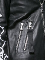 Edgy black leather motorcycle jacket with skull and crossbones sleeve design and metallic zipper and button detailing.