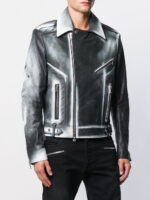 A person wears a black and silver gradient leather jacket with asymmetrical zippers and a structured collar, paired with black pants. The style is edgy and modern.