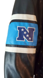 A close-up of a Vintage NFL Carolina Panthers Football Team Leather Jacket sleeve, showing a blue patch with a bold blue N and five white stars, outlined by white and blue stripes.