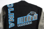 The Vintage NFL Carolina Panthers Varsity Jacket has a black body, gray sleeves, blue OLINA lettering, and PANTHERS text with a stadium graphic—perfect for any Carolina Panthers fan.