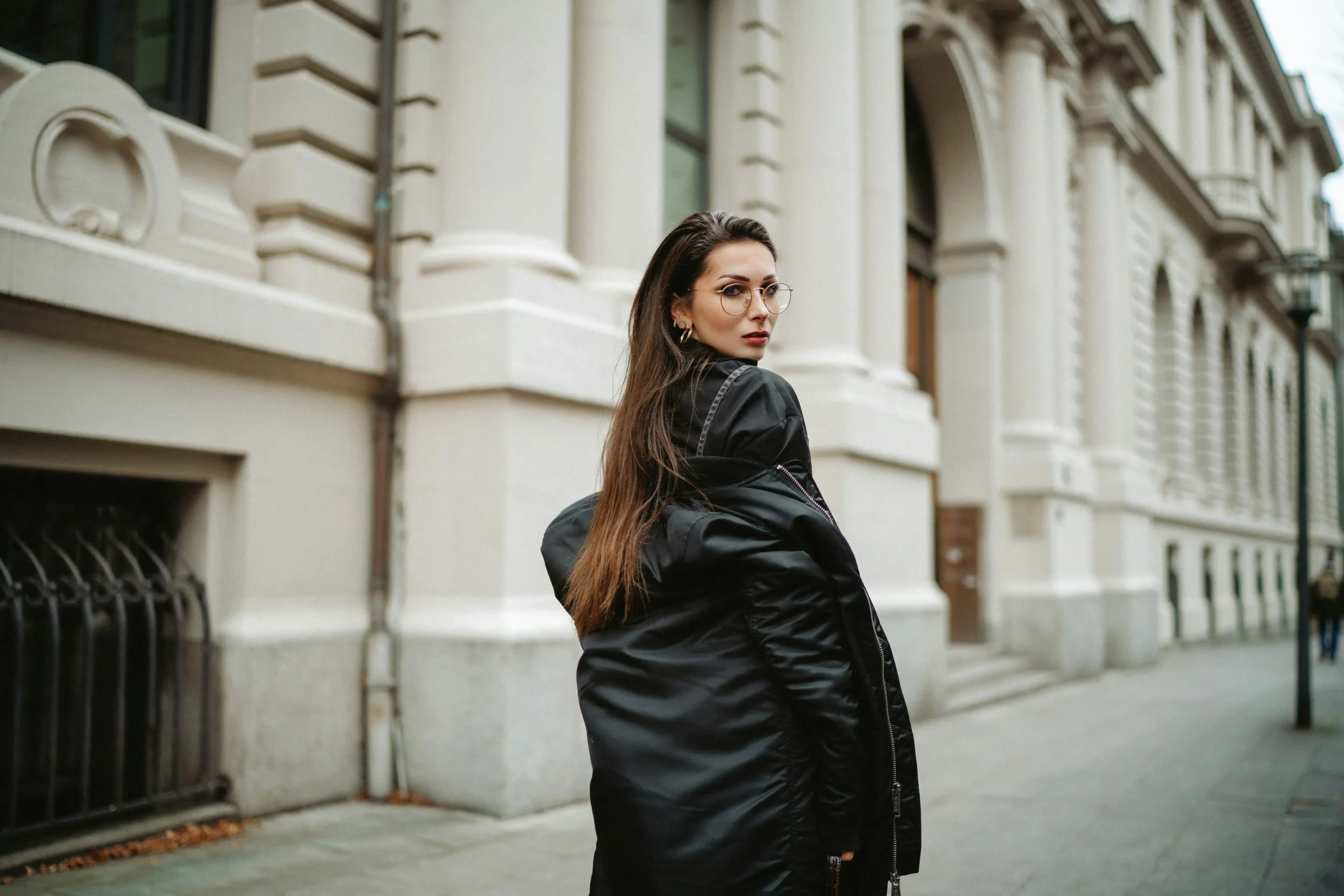 Women in black coat glancing back on a quiet city street.