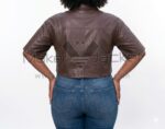 Back view of model wearing Brown Cropped Short Sleeve Leather Shirt featuring a horizontal seam detail, styled with high-waisted blue denim jeans.