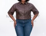 Front view of model wearing Brown Cropped Short Sleeve Leather Shirt with buttons and a front pocket, paired with high-waisted blue jeans against a white background